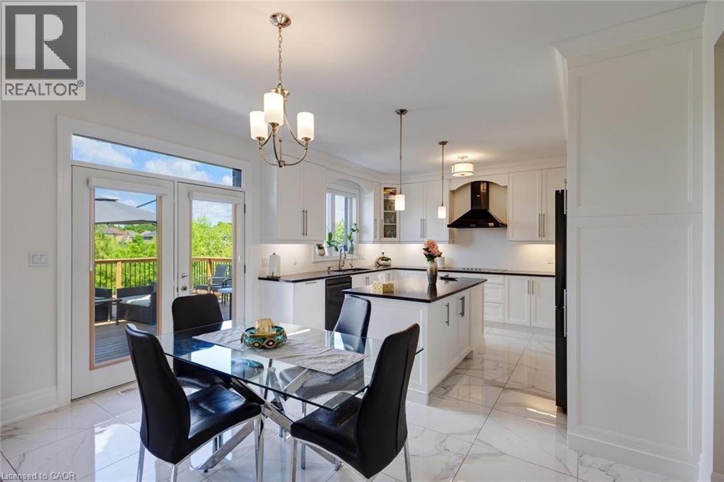 Open-concept kitchen and dining area featuring a central island with dark countertop, white cabinetry with under-cabinet lighting, a built-in oven hood, and light-toned tile flooring - 57 Hollybrook Trail, Kitchener, ON