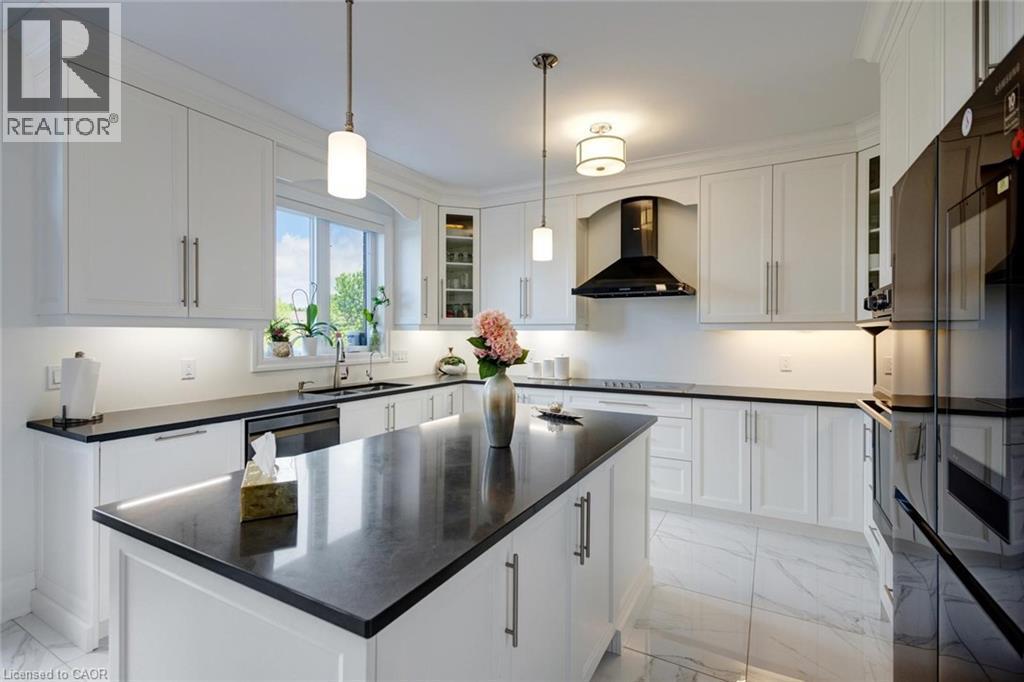 Kitchen featuring a central island with a dark countertop, white cabinetry with under-cabinet lighting, stainless steel appliances, and large format floor tiles - 57 Hollybrook Trail, Kitchener, ON