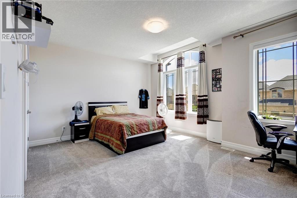 Spacious room featuring light gray carpeting, neutral wall paint, white trim, and multiple windows with white frames - 57 Hollybrook Trail, Kitchener, ON