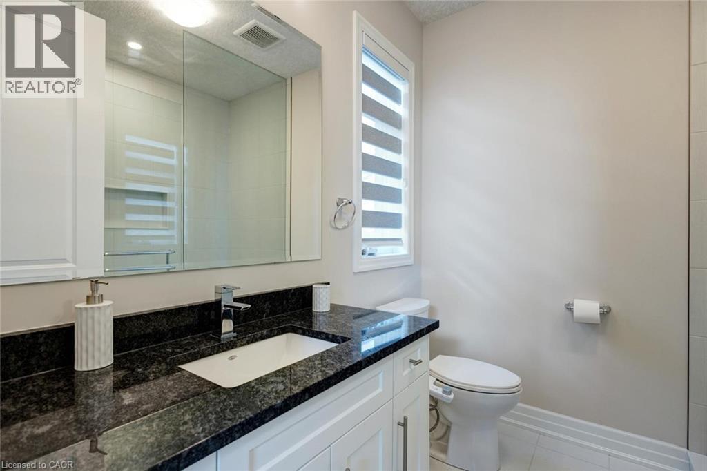 Bathroom featuring a white vanity with paneling, dark granite countertop, undermount rectangular sink, chrome faucet, and a large wall-mounted mirror - 57 Hollybrook Trail, Kitchener, ON