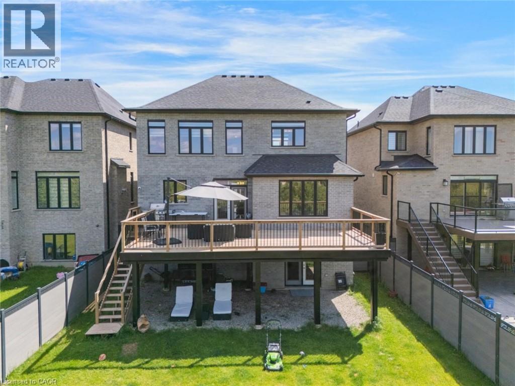 Rear exterior featuring a spacious elevated deck with wood railings, a lower-level concrete patio, a grass lawn, and a light-toned brick facade - 57 Hollybrook Trail, Kitchener, ON