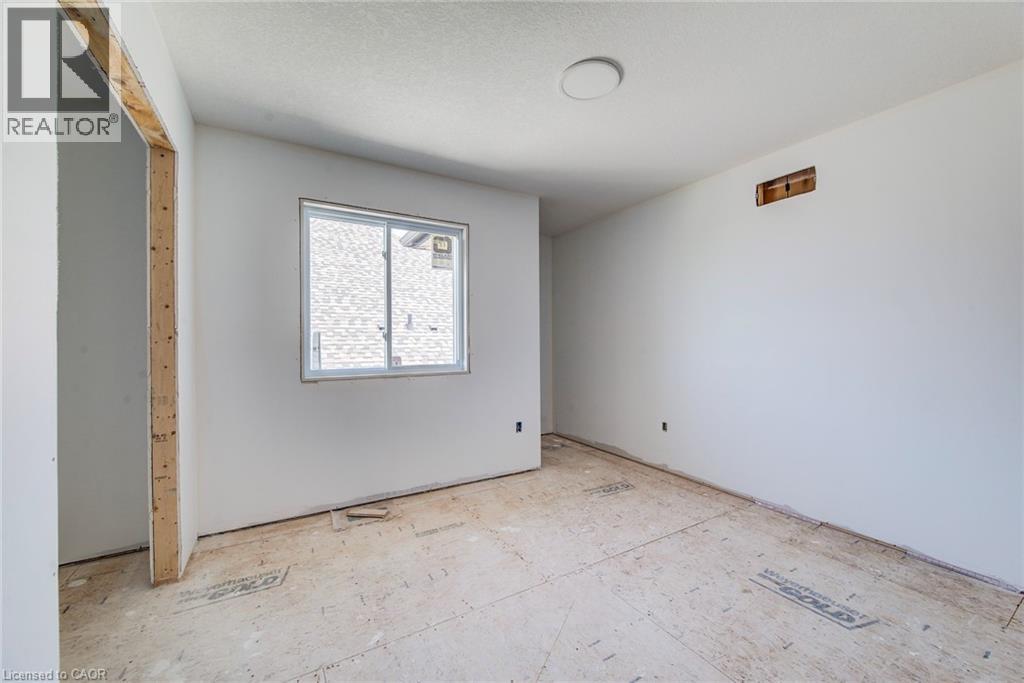 Unfinished interior space featuring a window with white framing, bare plywood subfloor, and a flush-mounted ceiling light fixture - 114 Bedell Drive, Mapleton, ON - Indoor Photo Showing Other Room