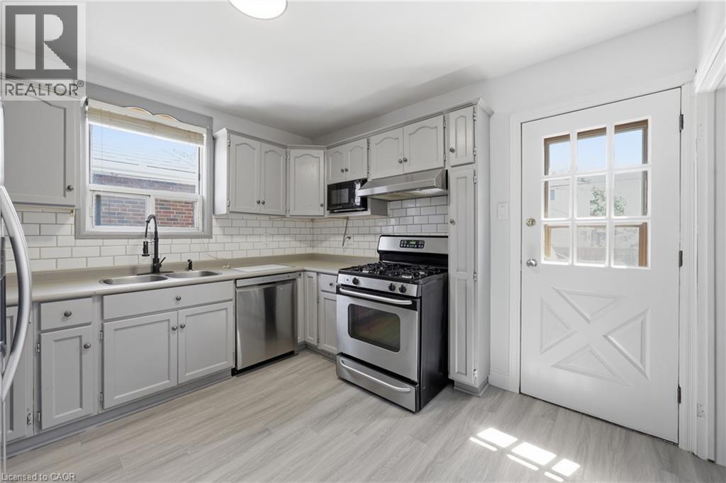 Kitchen featuring light gray cabinetry, white subway tile backsplash, stainless steel appliances, and wood-finish flooring - 97 Tragina Avenue S, Hamilton, ON