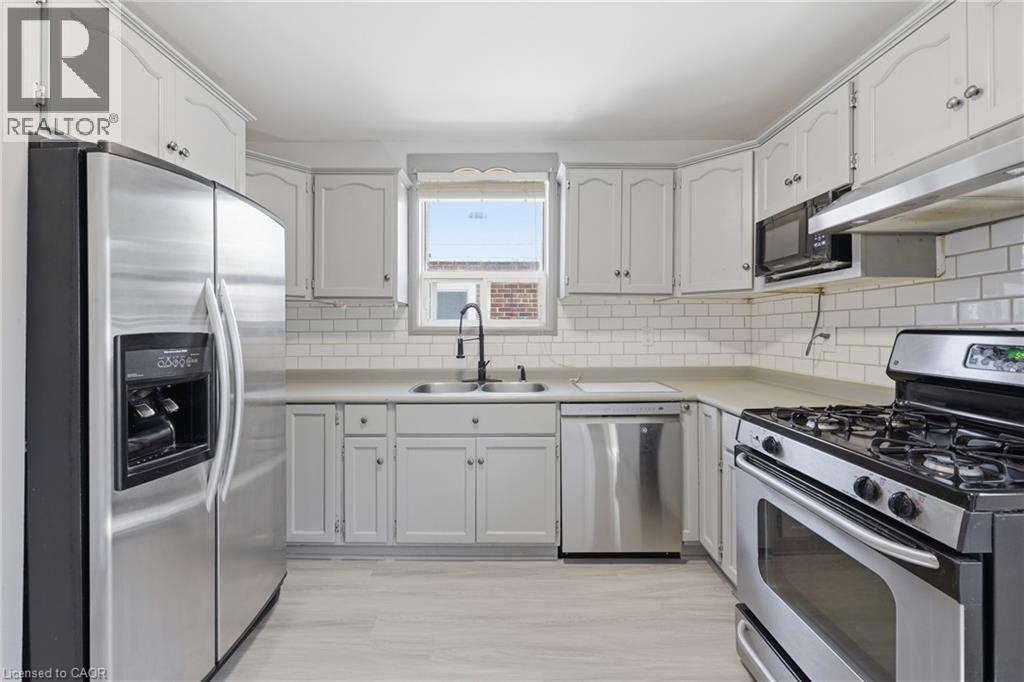 Kitchen featuring light-finish cabinetry, stainless steel appliances, subway tile backsplash, light-toned countertops, and wood-finish flooring - 97 Tragina Avenue S, Hamilton, ON