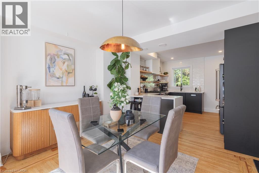 Open-concept dining area featuring a glass-top table, a contemporary pendant light fixture, and wood-finish flooring - 41 Park Row N, Hamilton, ON