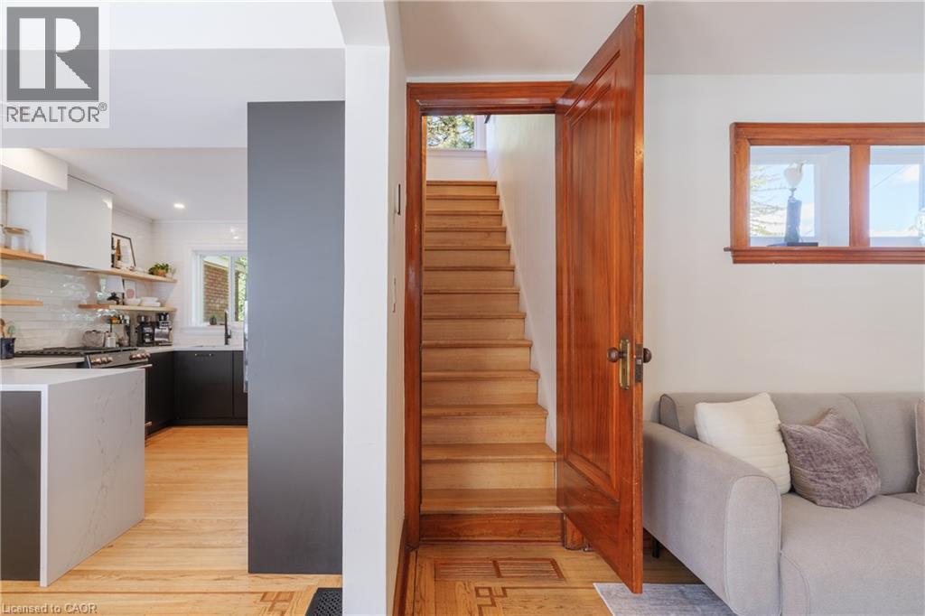 Hardwood staircase with a solid wood door, featuring a kitchen with a waterfall island, white subway tile backsplash, and floating shelves - 41 Park Row N, Hamilton, ON