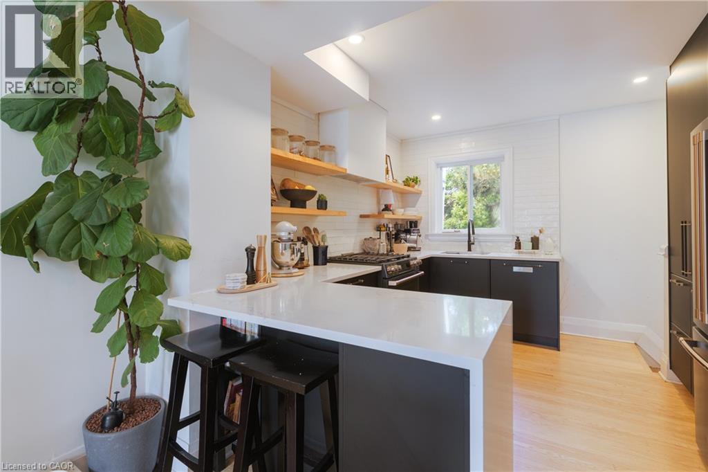 Modern kitchen featuring a waterfall island with counter seating, black base cabinetry, open wood shelving, a white subway tile backsplash, and light wood-finish flooring - 41 Park Row N, Hamilton, ON