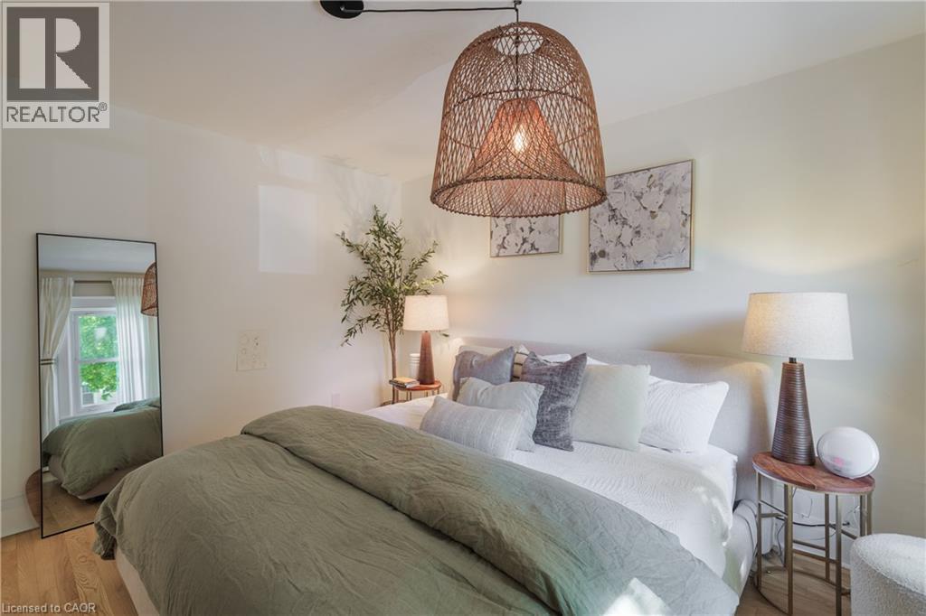 Bedroom featuring wood-finish flooring, a woven pendant light fixture, and a window with natural light - 41 Park Row N, Hamilton, ON