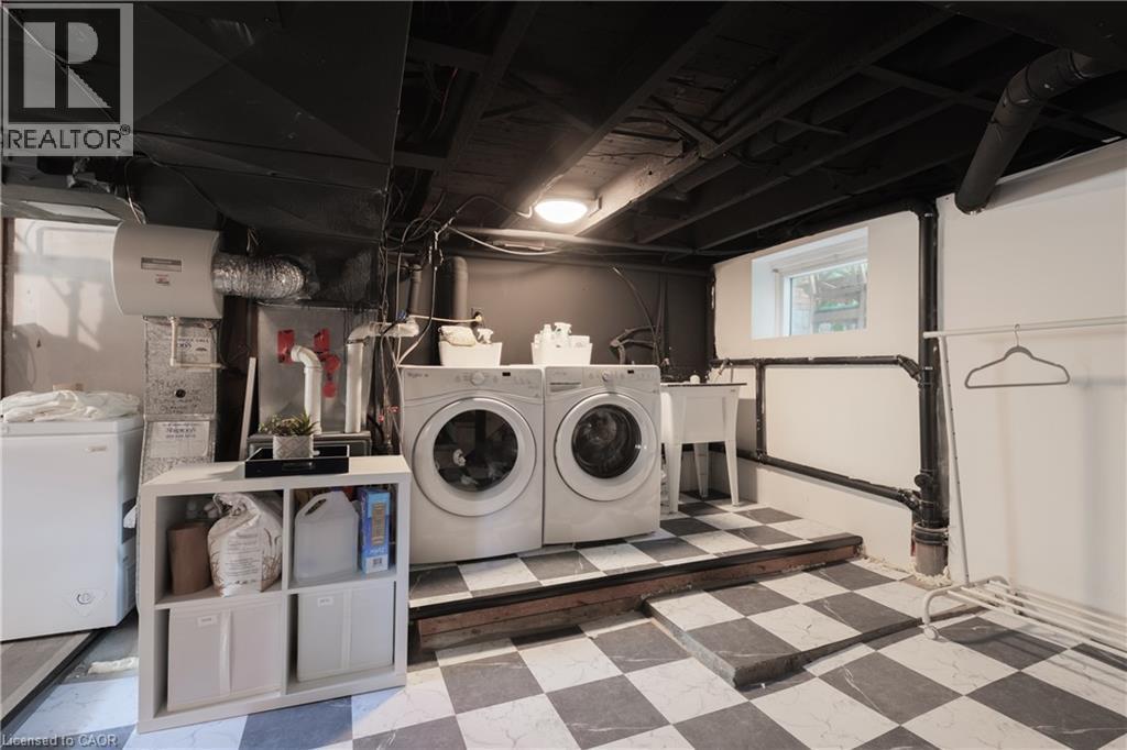 Utility area featuring checkerboard flooring, a window, and exposed overhead pipes - 41 Park Row N, Hamilton, ON