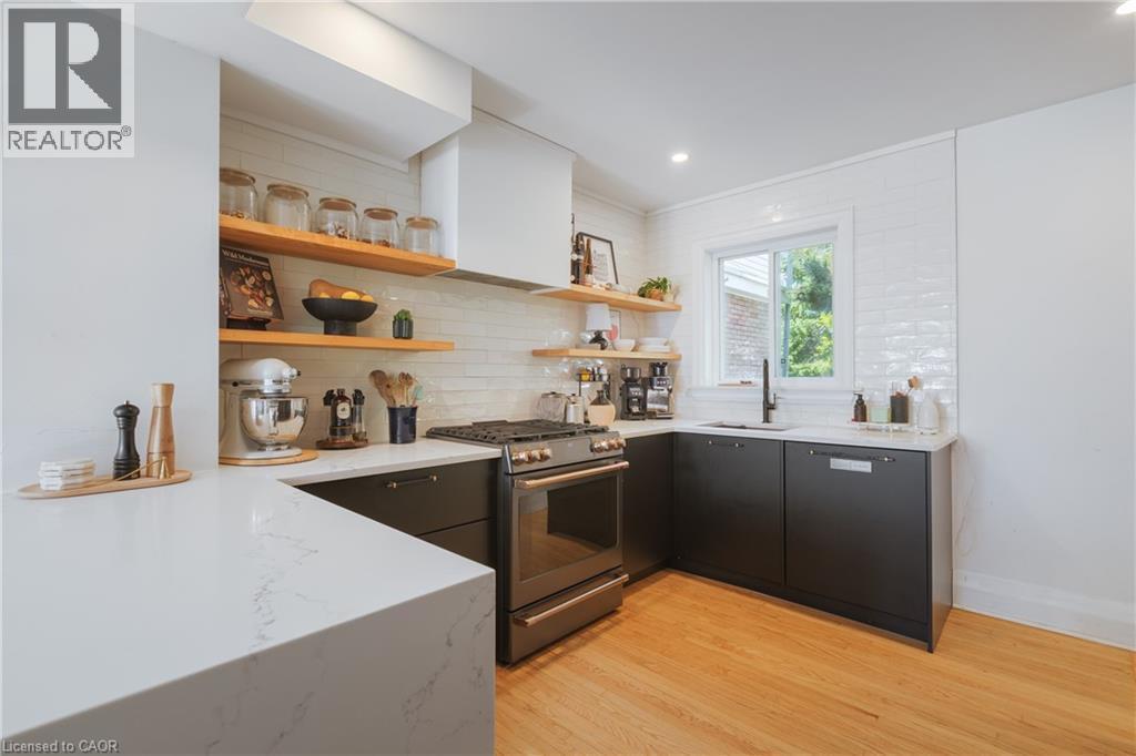 Modern kitchen featuring light wood-finish flooring, dark cabinetry, and white quartz countertops - 41 Park Row N, Hamilton, ON