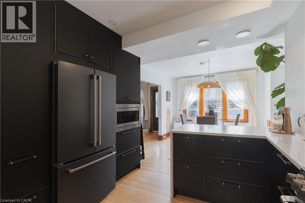 Modern kitchen featuring black cabinetry, stainless steel appliances, light wood-finish flooring, and white countertops - 41 Park Row N, Hamilton, ON