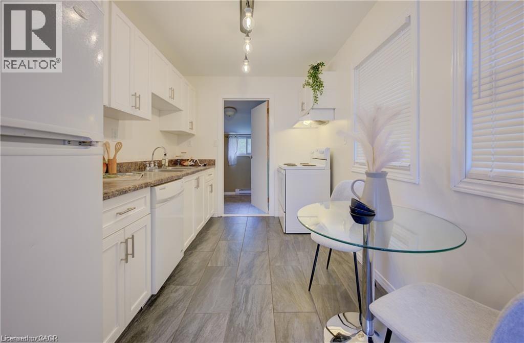 Galley kitchen featuring white cabinetry, stone-look countertops, and wood-finish flooring - 73 East 33Rd Street, Hamilton, ON