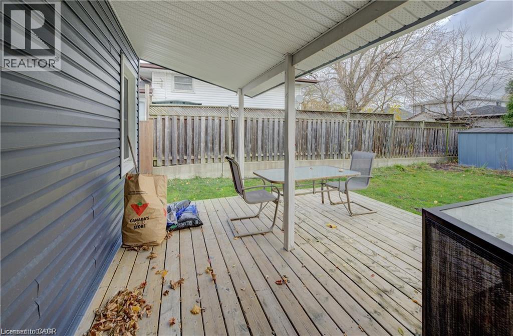 Expansive wooden deck with a covered patio area, featuring a slatted privacy fence, green lawn space, and an exterior storage shed - 73 East 33Rd Street, Hamilton, ON