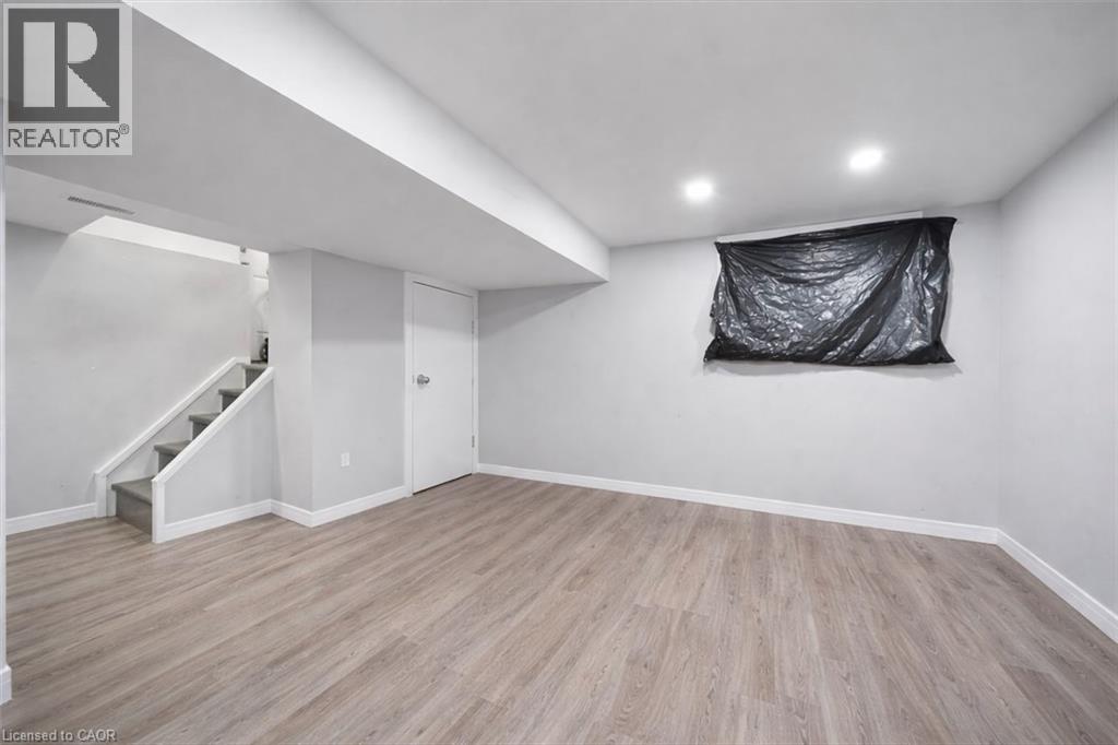 Spacious room featuring wood-finish flooring, recessed lighting, and a white interior door - 106 Lottridge Street, Hamilton, ON