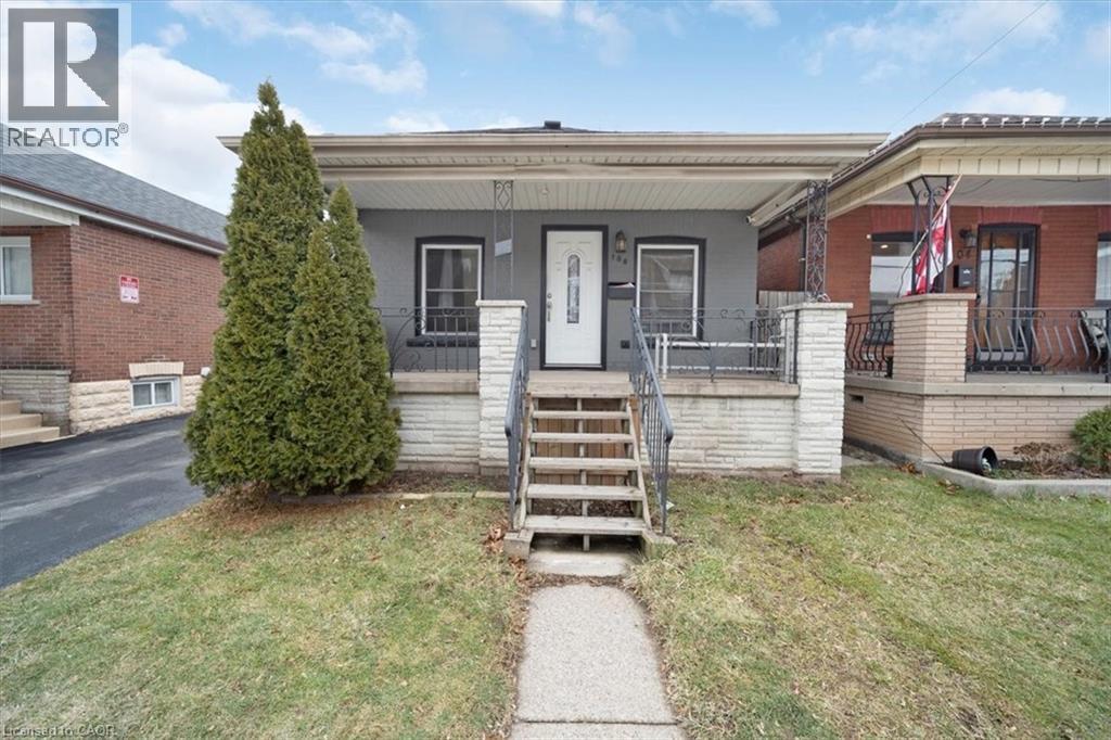 Grey exterior with white trim, featuring a covered porch with decorative railing and a white entry door - 106 Lottridge Street, Hamilton, ON