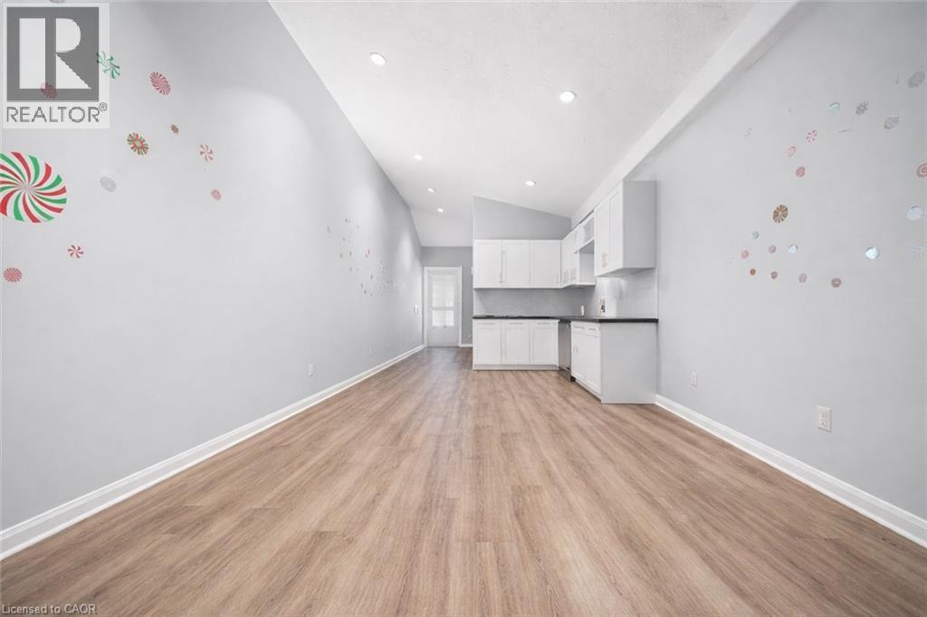Expansive open-concept living area featuring wood-finish flooring, recessed lighting, and a modern kitchen with white cabinetry and dark countertops - 106 Lottridge Street, Hamilton, ON