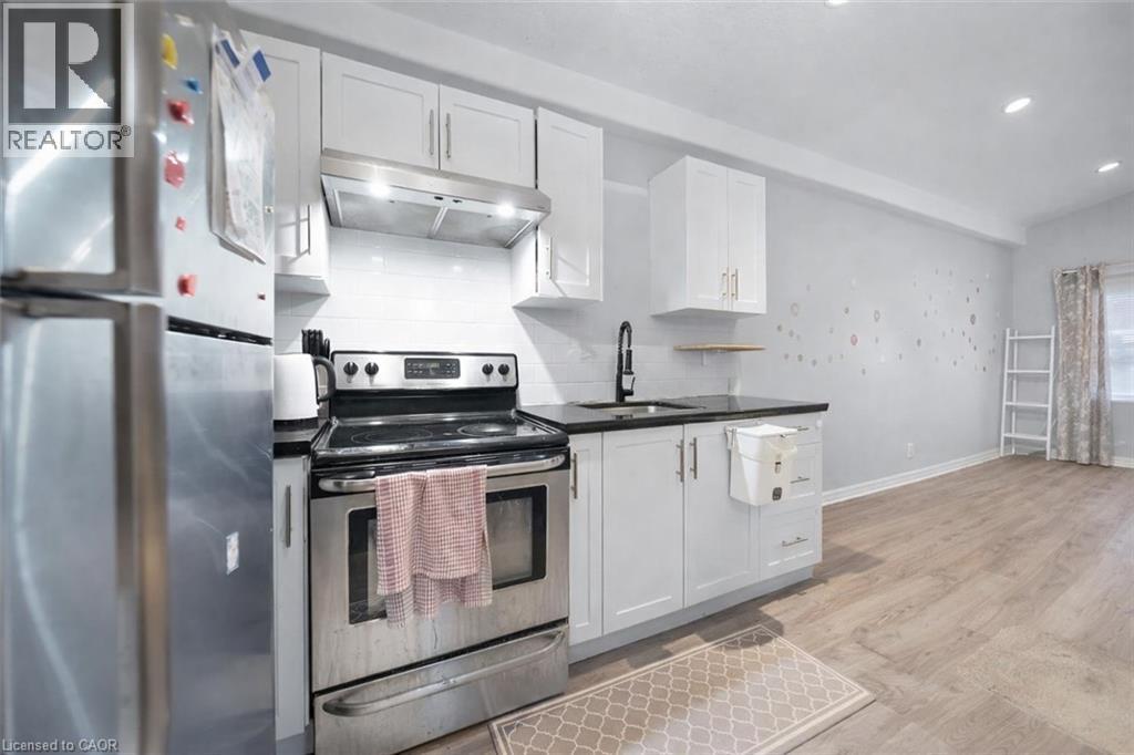 Compact kitchen featuring white cabinetry, black countertops, stainless steel appliances, and a subway tile backsplash - 106 Lottridge Street, Hamilton, ON