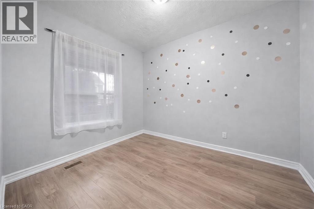 Room featuring wood-finish flooring, a window with a sheer curtain, and light grey walls - 106 Lottridge Street, Hamilton, ON