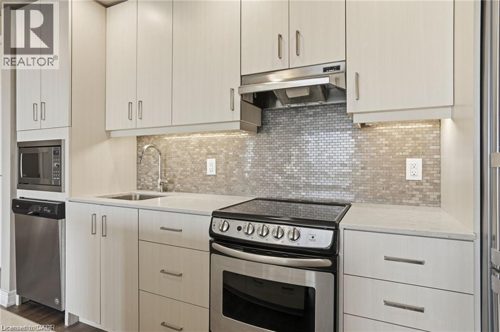 Modern kitchen featuring light wood-finish cabinetry, stainless steel appliances, a tile mosaic backsplash, under-cabinet lighting, and light-toned countertops - 40 Esplanade Lane Unit# 614, Grimsby, ON