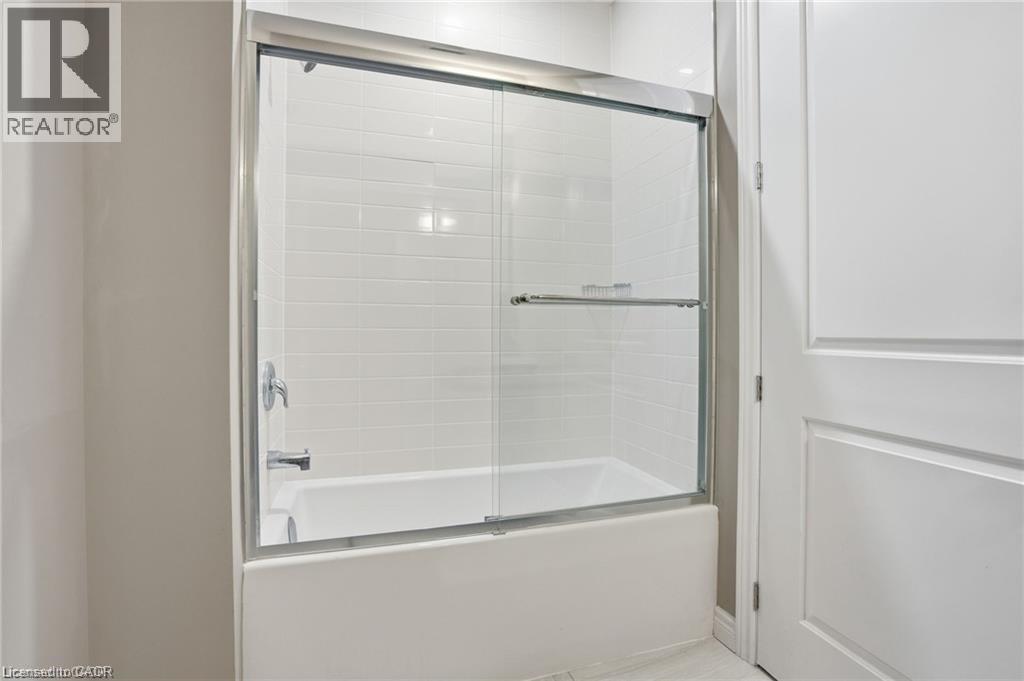 White bathtub and shower combination featuring subway tile surround, chrome fixtures, and a sliding glass enclosure - 40 Esplanade Lane Unit# 614, Grimsby, ON