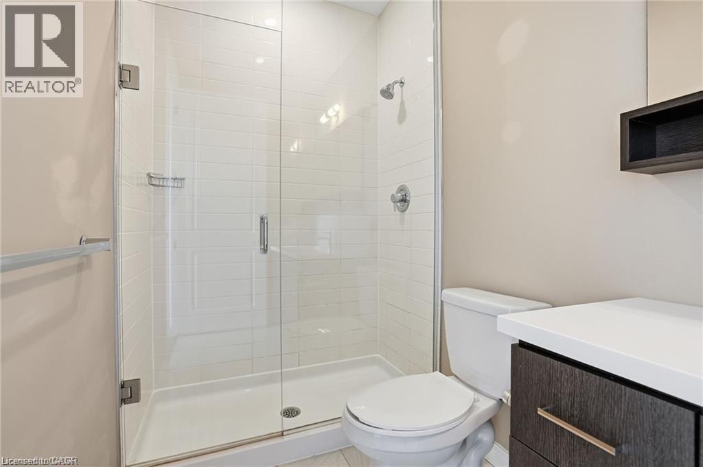 Bathroom featuring a glass-enclosed shower with white subway tile, a dark wood-finish vanity with a light-toned countertop, and chrome fixtures - 40 Esplanade Lane Unit# 614, Grimsby, ON