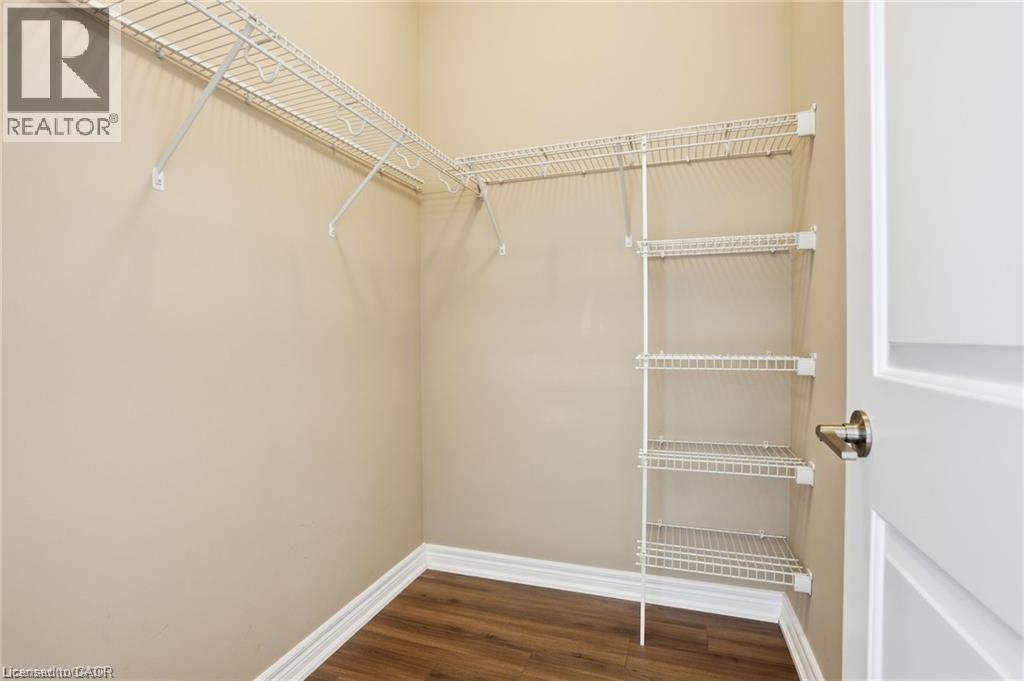 Walk-in closet featuring organized wire shelving, perimeter hanging rods, wood-finish flooring, and light neutral wall paint - 40 Esplanade Lane Unit# 614, Grimsby, ON
