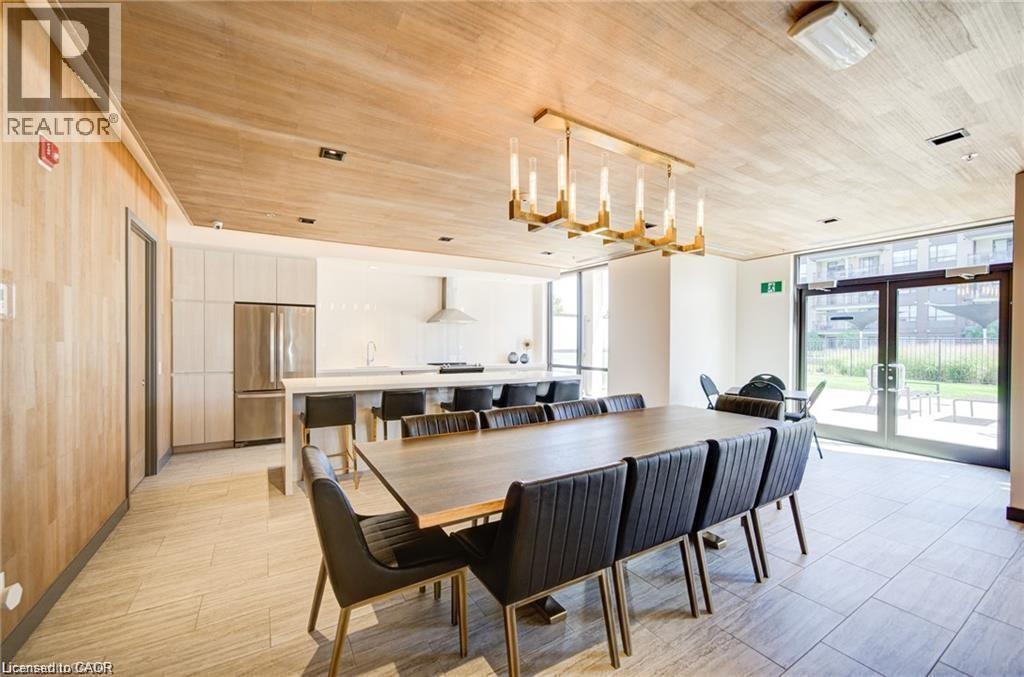 Modern dining area featuring a large rectangular table with seating for eight, illuminated by a contemporary gold-finish chandelier - 40 Esplanade Lane Unit# 614, Grimsby, ON