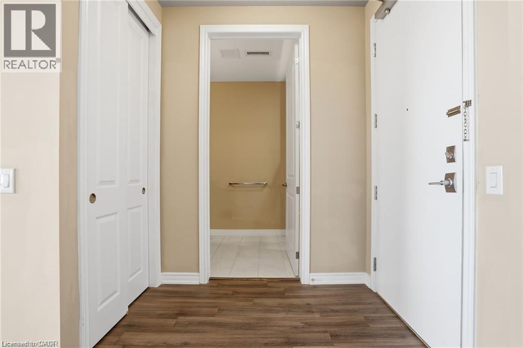 Entryway with wood-finish flooring, a white paneled closet door, and a solid white entrance door with modern hardware - 40 Esplanade Lane Unit# 614, Grimsby, ON