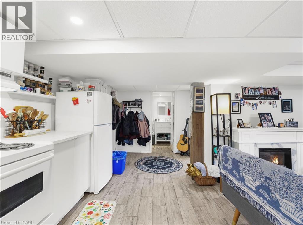 Open-concept living area featuring wood-finish flooring, a white kitchen with appliances, and a built-in fireplace with a white mantel - 420 Waverly Street, Hamilton, ON