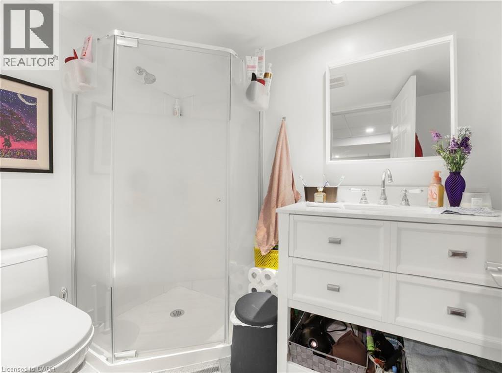 Modern basement bathroom featuring a glass-enclosed shower with a chrome showerhead, a white toilet, and a white vanity with an integrated sink and chrome fixtures - 420 Waverly Street, Hamilton, ON