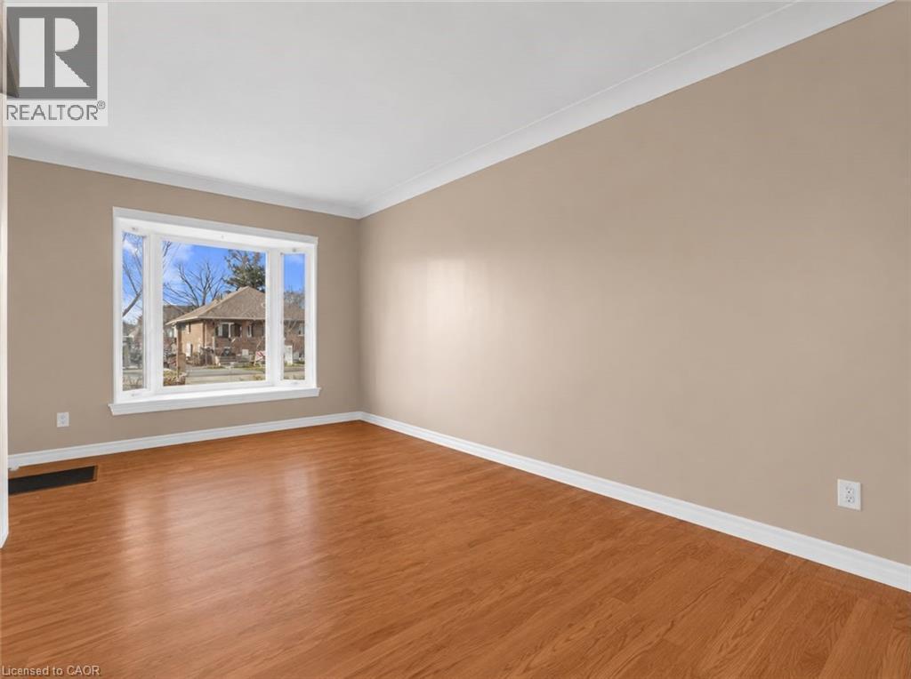 Bright interior room featuring a large bay window, wood-finish flooring, neutral wall paint, and white crown molding - 420 Waverly Street, Hamilton, ON