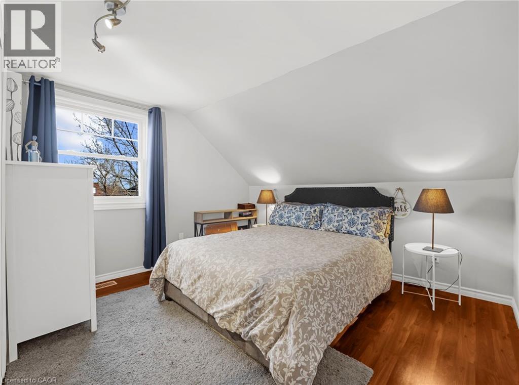 Bedroom featuring sloped ceilings, hardwood flooring, and a large window with blue drapes - 420 Waverly Street, Hamilton, ON