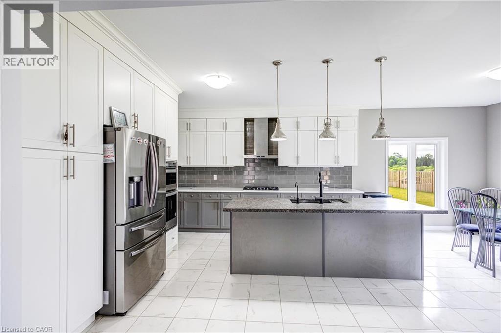 Bright kitchen featuring a central island, white shaker cabinetry, stainless steel appliances, and a gray subway tile backsplash - 417 Rivertrail Avenue, Kitchener, ON
