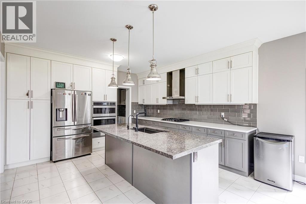 Contemporary kitchen featuring a large central island with a sink, stainless steel appliances, white cabinetry, a gray subway tile backsplash, and light-toned tile flooring - 417 Rivertrail Avenue, Kitchener, ON