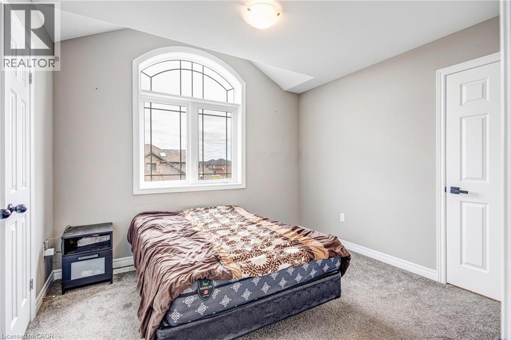Arched window with decorative grilles, light gray painted walls, textured gray carpeting, white trim, and white panel doors with black hardware - 417 Rivertrail Avenue, Kitchener, ON