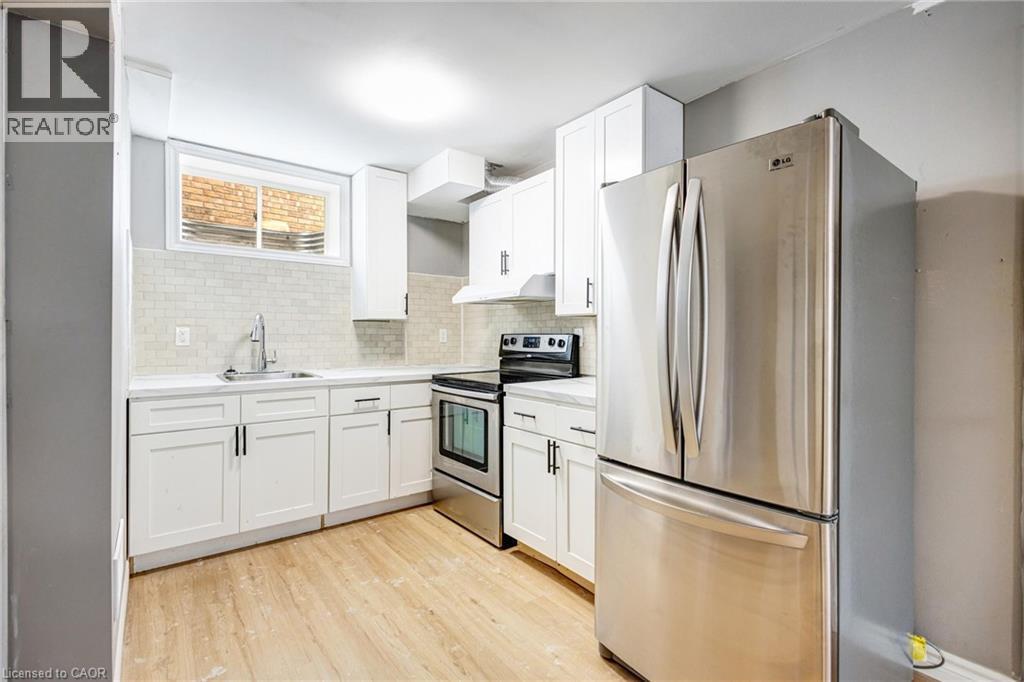 Kitchen featuring white shaker-style cabinetry, stainless steel appliances, light wood-finish flooring, a white subway tile backsplash, and a contemporary sink with a gooseneck faucet - 417 Rivertrail Avenue, Kitchener, ON