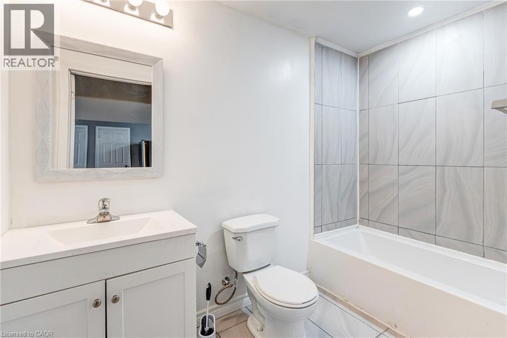Bathroom featuring a white vanity with integrated sink, a rectangular mirror with a patterned frame, a toilet, a bathtub, and tiled shower walls - 417 Rivertrail Avenue, Kitchener, ON