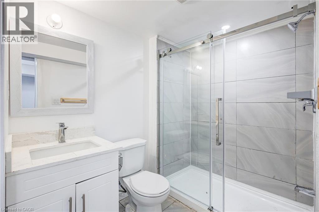 Contemporary bathroom featuring a glass-enclosed shower with tile surround, white vanity with integrated sink and chrome faucet, and a frameless mirror - 417 Rivertrail Avenue, Kitchener, ON