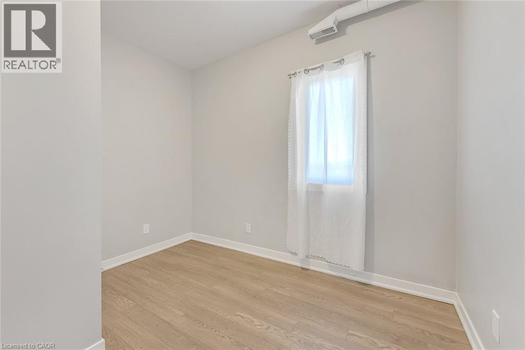 Light-filled interior featuring wood-finish flooring, white baseboards, and a window with a sheer curtain - 657 Barton Street E Unit# 302, Hamilton, ON