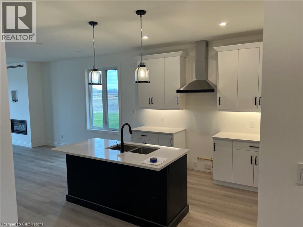Kitchen featuring wall chimney range hood, a sink, light wood-style flooring, decorative light fixtures, and a center island with sink - 207 Arden Crescent Unit# Upper Level, Mitchell, ON