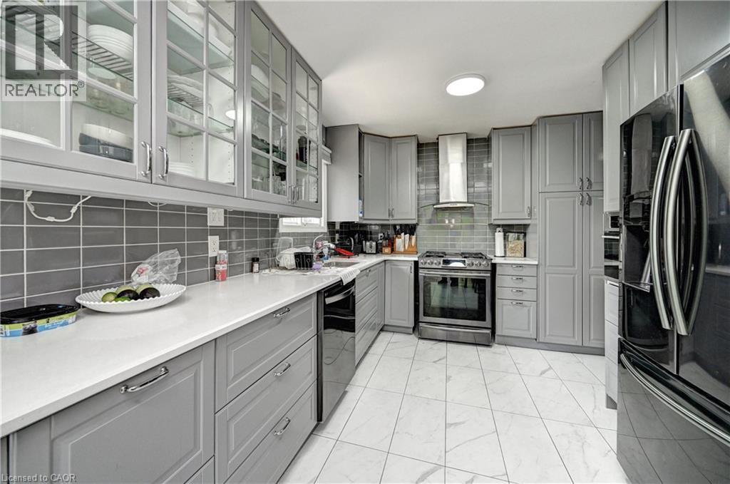 Contemporary kitchen featuring gray cabinetry with glass-front upper cabinets, white countertops, and a subway tile backsplash - 525 Fallingbrook Drive, Waterloo, ON