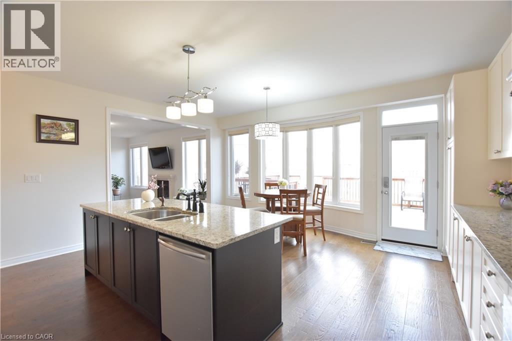 Kitchen featuring light stone countertops, stainless steel dishwasher, an island with sink, hanging light fixtures, and dark wood finished floors - 512 Terrington Crescent, Kitchener, ON