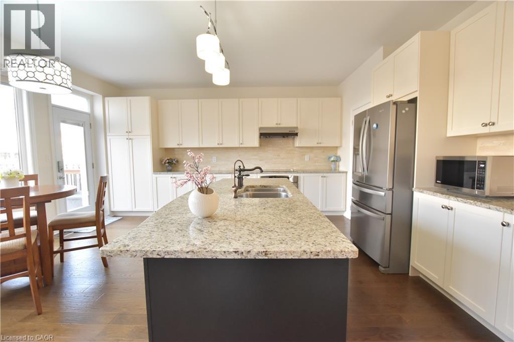 Dual tone kitchen featuring stainless steel appliances, dark wood-type flooring, light stone counters, hanging light fixtures, and two tone cabinets - 512 Terrington Crescent, Kitchener, ON