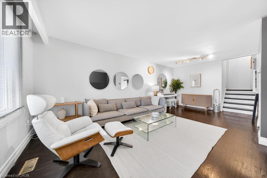 Bright living area featuring dark wood-finish flooring, white walls, and a staircase with dark treads and risers - 19 Glen Forest Drive, Hamilton, ON