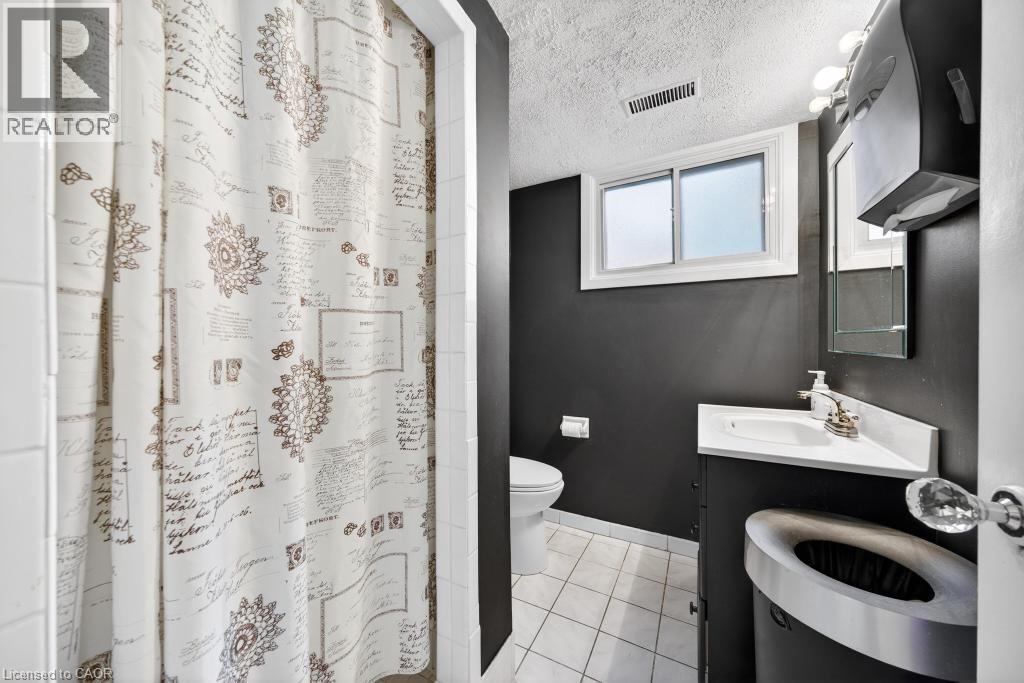 Bathroom featuring a corner vanity with an integrated sink, a window with white trim, and white tile flooring - 19 Glen Forest Drive, Hamilton, ON