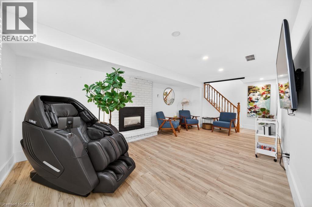 Spacious room featuring light wood-finish flooring, a white brick fireplace with a dark insert, recessed lighting, and a wood staircase with balusters - 19 Glen Forest Drive, Hamilton, ON
