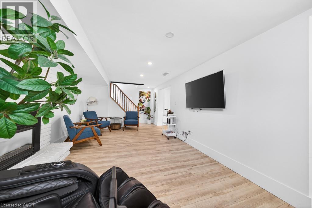 Spacious interior showcasing wood-finish flooring, a contemporary fireplace with a white painted brick surround, recessed lighting, and a staircase with a dark railing - 19 Glen Forest Drive, Hamilton, ON