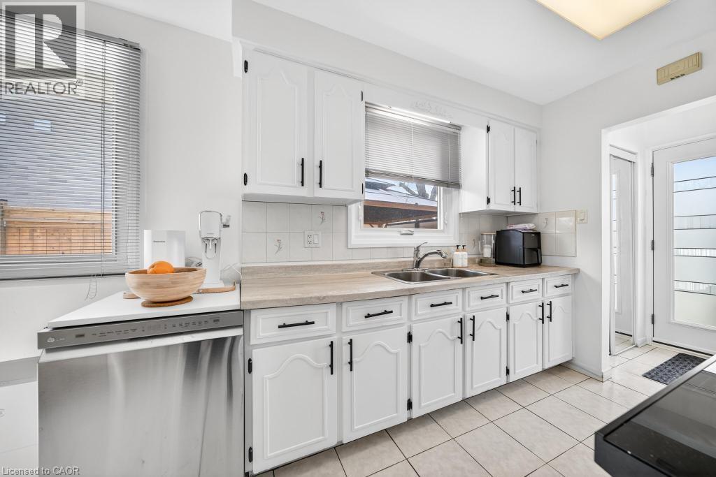 Kitchen featuring white cabinetry, light-toned countertops, a double basin sink, and tile flooring - 19 Glen Forest Drive, Hamilton, ON