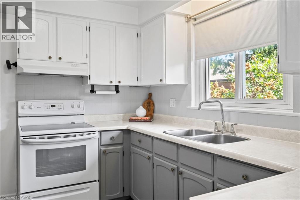 Kitchen featuring two-tone cabinetry with white upper cabinets and grey lower cabinets, a dual basin stainless steel sink with a chrome faucet, light-toned countertops, and a white electric range with - 1083 Melton Drive, Mississauga, ON