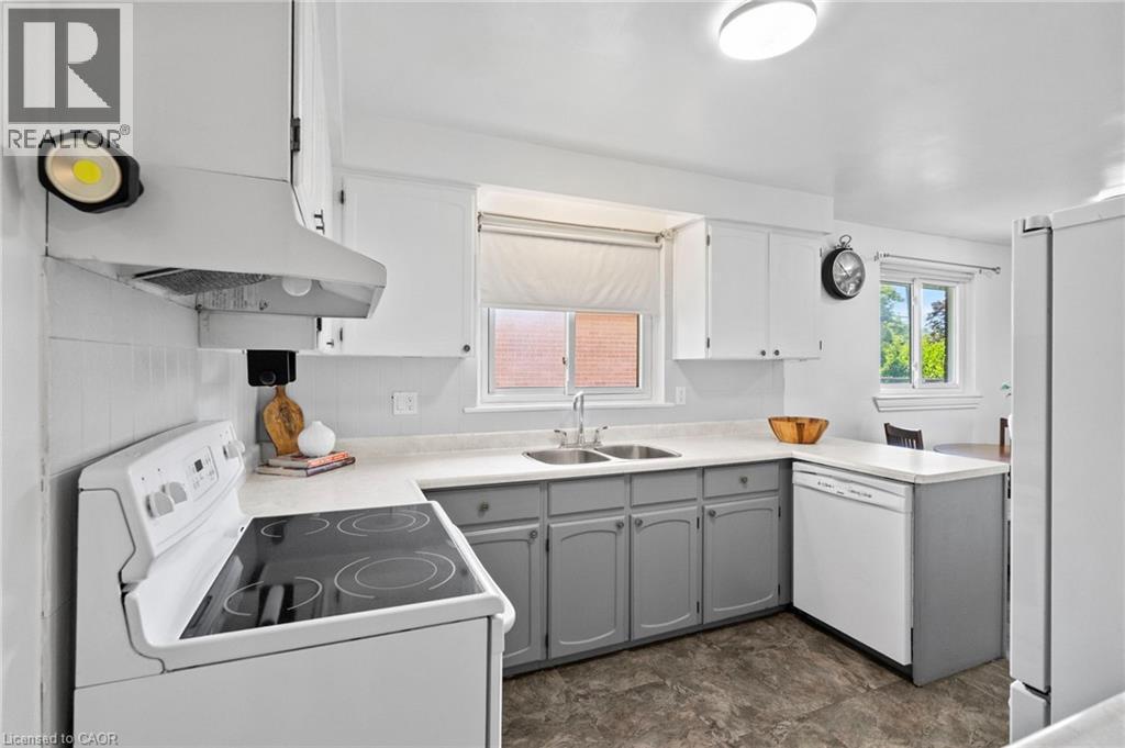 Kitchen featuring a dual-tone cabinetry with white upper cabinets and gray lower cabinets, a white electric range with a hood fan, a double basin stainless steel sink, a white dishwasher, and durable - 1083 Melton Drive, Mississauga, ON